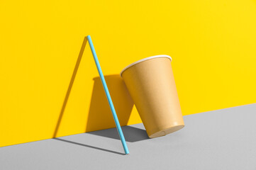 Eco friendly stripped paper straw and cup leaning against the color wall. Recycling, biodegradable concept. Minimal geometric scene