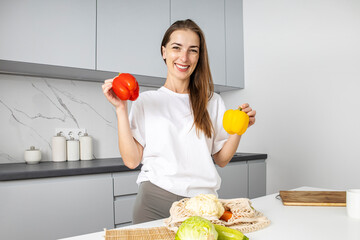 Fototapeta premium Smiling young woman laying out purchases from the store in the kitchen