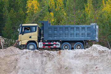 Empty dump truck on a clay quarry next to the autumn forest