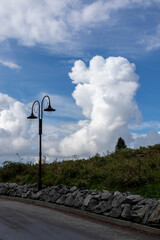 Forests at the top of Równica under a sky with large white clouds with a street lamp in the foreground