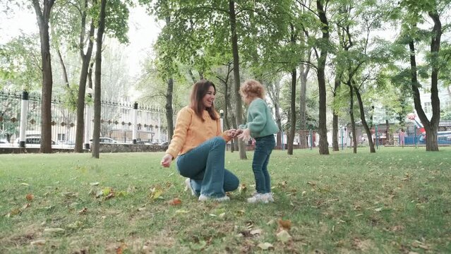 Loving mother walks with her cute daughter in the park. Mom and little daughter hold autumn leaves in their hands, throw them up and rejoice. loving family
