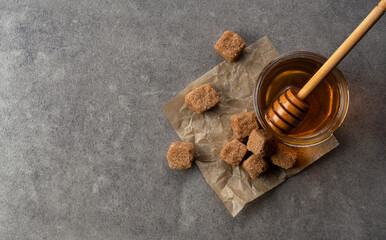 Brown sugar with honey and wooden honey dipper on stone background.
