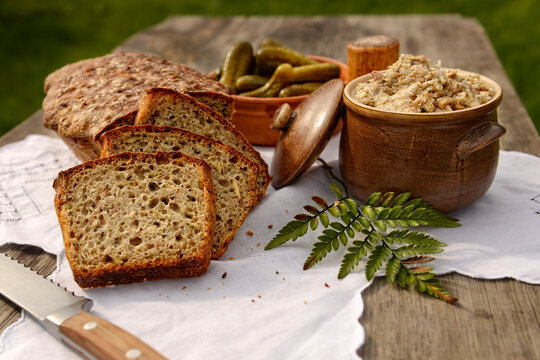 Wiejski stół — bochenek chleba pokrojony w kromki, ogórki kiszone i smalec domowej roboty