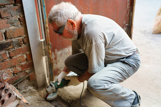 elderly gray-haired man in gloves cleans the metal structure from rust. 