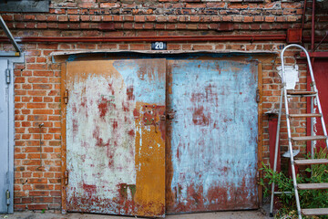 old metal brick garage door with stripped paint and ladder stepladder.