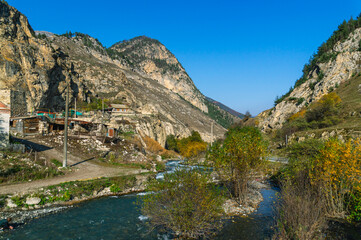 Autumn landscape in the mountains. Yellowed trees in autumn in the mountains of North Ossetia. Mountain gorges. View of the mountain peaks. A village in the mountains and a mountain river.