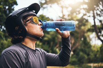 Cyclist, water and bottle in forest for hydration, with cycling equipment and sunglasses by trees for wellness. Man, drink and sports while exercise, workout or training for fitness outside in woods