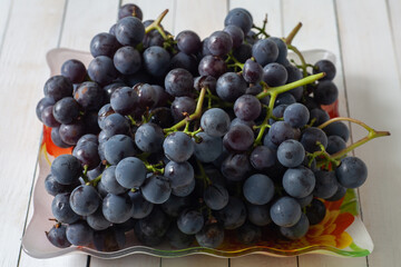 There are grapes in a plate on the table. Horizontal shot.