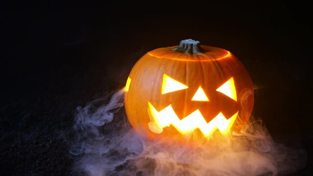 A Halloween pumpkin with a colored light inside is lying on the black ground.
