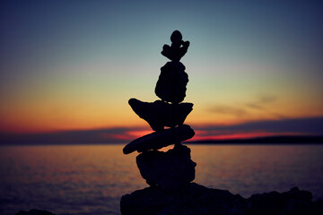 Silhouette of balanced zen stones on the ocean beach at sunset sunrise time.