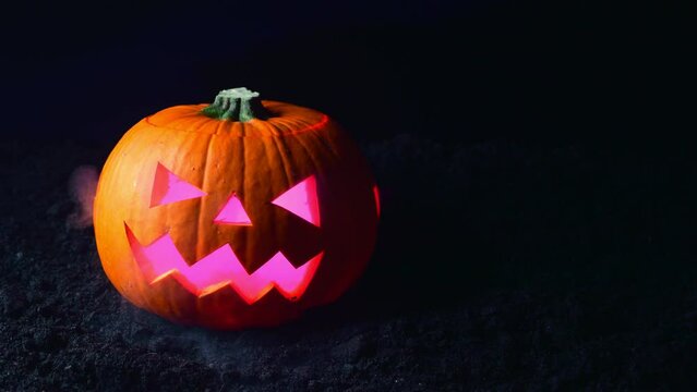 A pumpkin with its face cut out releases heavy smoke onto black ground. Halloween background.