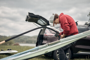 Windsurfer and camper packing and unpacking from a car in nature.