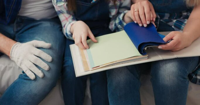 Children's hands holding a folder with a color palette. A girl with brown hair, wearing denim overalls and a checked shirt, is choosing a color for future nursery.