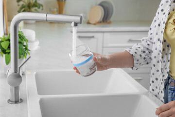 Woman filling glass with water from tap in kitchen, closeup
