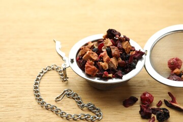 Snap infuser with dried herbal tea leaves and fruits on wooden table, closeup