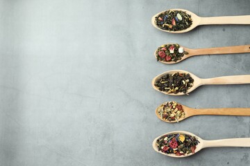 Different kinds of dry herbal tea in wooden spoons on light grey table, flat lay. Space for text