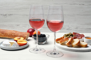 Glasses of delicious rose wine and snacks on white wooden table