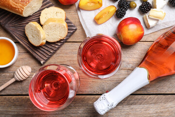 Delicious rose wine and snacks on wooden table, flat lay