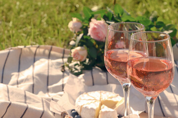 Glasses of delicious rose wine, flowers and food on picnic blanket outdoors