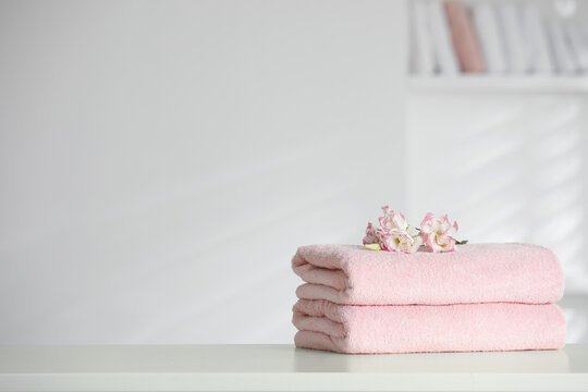 Stack of clean soft towels with eustoma flowers on white table indoors. Space for text