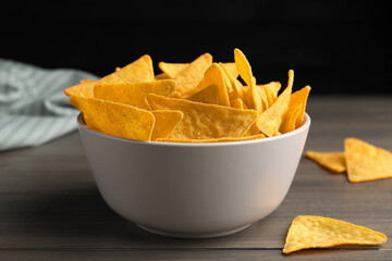 Tortilla chips (nachos) in bowl on wooden table against dark background, closeup