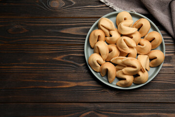 Tasty fortune cookies with predictions in plate on wooden table, top view. Space for text