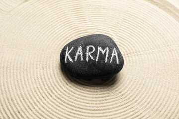 Stone with word Karma and circles on sand, top view