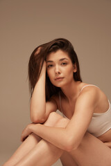 Naklejka premium Portrait of young beautiful woman posing in underwear isolated over dark beige studio background. Femininity. Self-love