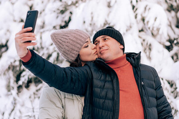 Young couple in love take a selfie on a smarfton while walking in the winter forest.Winter activities,active lifestyle,Valentine's day,tenderness and love.