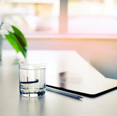 working place with glass of water and tablet against windon