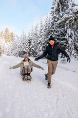 Young couple in love is sledding in a winter forest and having fun spending time together.Winter,active lifestyle,Valentine's day,newlyweds,tenderness and love.Selective focus.
