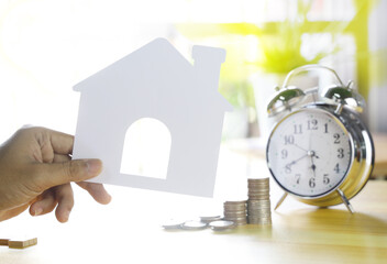 Hand hold house paper with coin and alarm clock.Plan to buy a house concept.