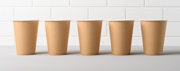 Row of biodegradable craft paper cups on white background. Eco friendly take away cups for coffee. Banner.