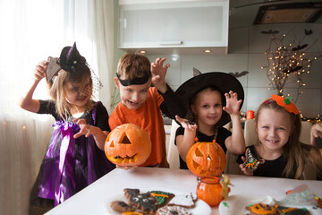 group of children in masquerade costumes  paint gingerbread for the halloween holiday at home in the kitchen. Halloween party
