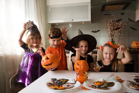group of children in masquerade costumes  paint gingerbread for the halloween holiday at home in the kitchen. Halloween party
