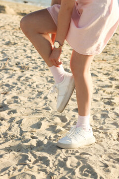 Legs of a girl in a skirt in fashionable sneakers on the sand, the image is taken for a walk.