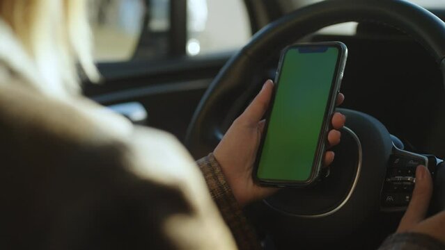 Close-up of a woman holding a mobile phone with a green screen in her hands while sitting in a car