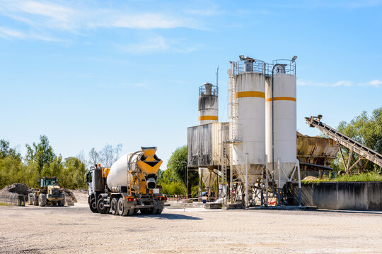 A concrete mixer truck and a wheel loader are parked next to sand silos in a quarry on a sunny day.