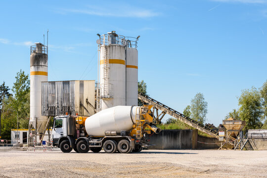A concrete mixer truck is parked next to a sand silo in a quarry on a sunny day.