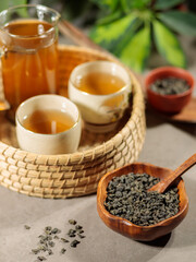 Green tea in a glass teapot and two Japanese porcelain cups on a wicker tray. Close-up
