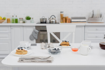 Fototapeta na wymiar Tasty pancakes with blueberries near coffee and smartphone in kitchen.