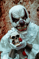scary evil clown with a skull in his hands