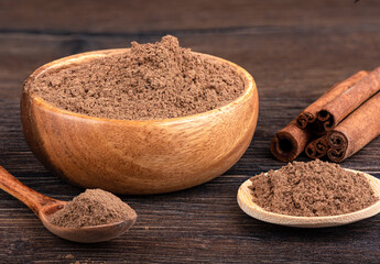 Cinnamon sticks and ground cinnamon in a bowl, on a spoon over a wooden background.