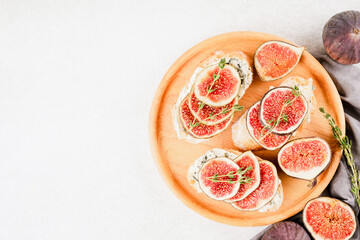 Healthy quick breakfast recipe - fresh bruschetta with ripe fig, blue and cream cheese and herbs over white concrete table background with copy space. Top view, selective focus