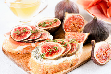 Bruschetta with raw ripe fig, blue and cream cheese, prosciutto, walnuts and herbs on wooden serving board. Healthy quick breakfast idea. Italian cuisine. Selective focus