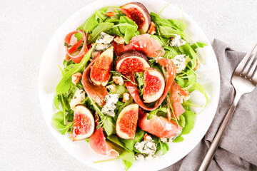 Healthy food recipe - salad with fresh fig, blue cheese, prosciutto, arugula and spinach on white table background with copy space. Lunch idea. Top view. Selective focus