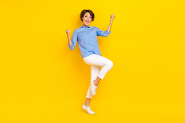Full length photo of lucky excited girl dressed blue shirt rising fists screaming isolated yellow...