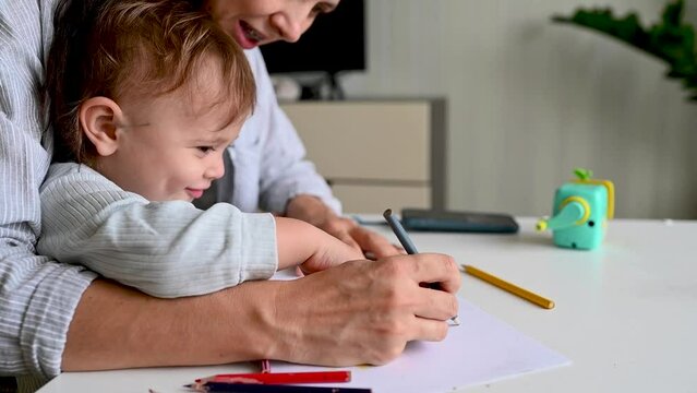 Mother and child sit at the table and draw with colored pencils
