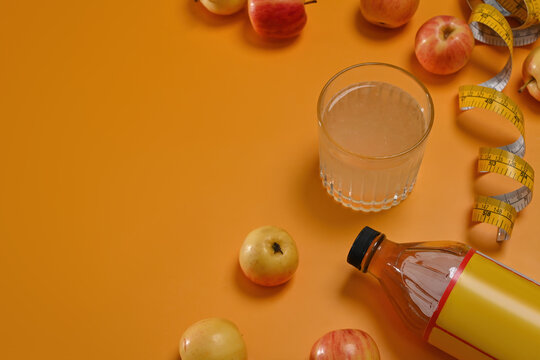 Apple cider vinegar in glass and bottle, fresh red apples and measuring tape on yellow background, Top view, Copy space.