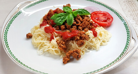 Bolognese meat-based sauce with pasta. Pasta with minced meat, tomato spicy sauce garnished with green fresh basil leaves. Dish served in the big white plate